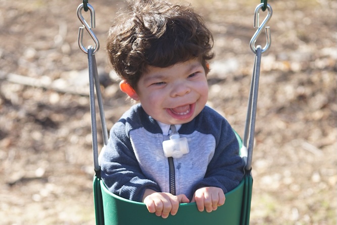 Little boy sitting in a swing outside in a park