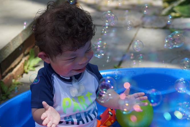 Little boy sitting in a kiddie pool with bubbles