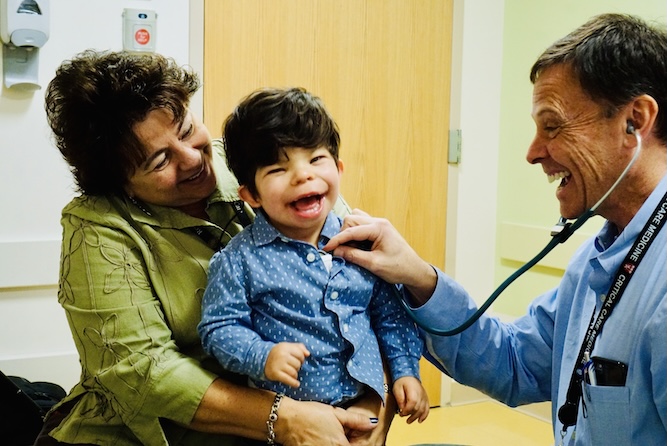 Doctor listening to a little boy's heart beat while being held by a woman