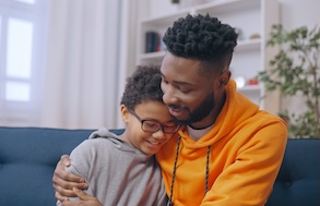 Man hugging boy sitting on the couch